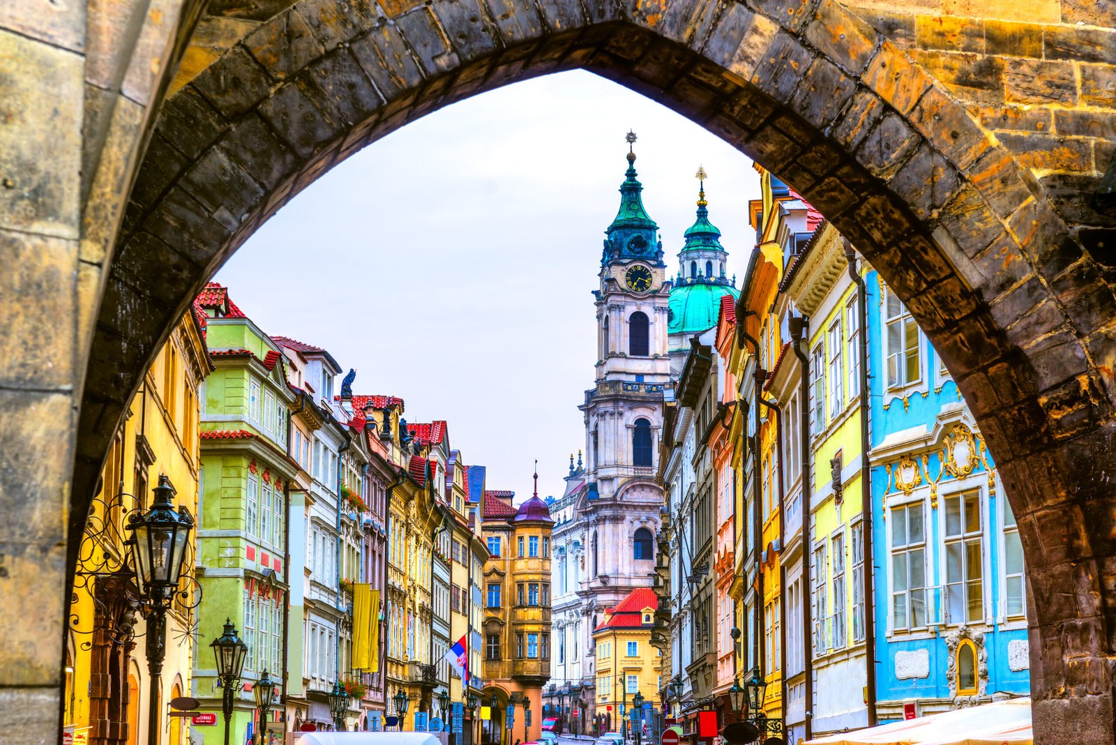 View of St. Nicholas Church and colorful baroque buildings in Malá Strana, Prague, framed by a stone arch