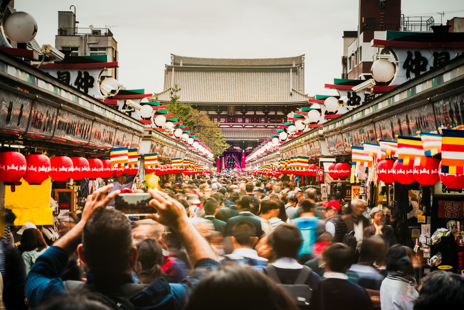 Crowds walking along Nakamise Shopping Street in Asakusa, Tokyo, with food and souvenir stalls leading toward Sensō-ji Temple