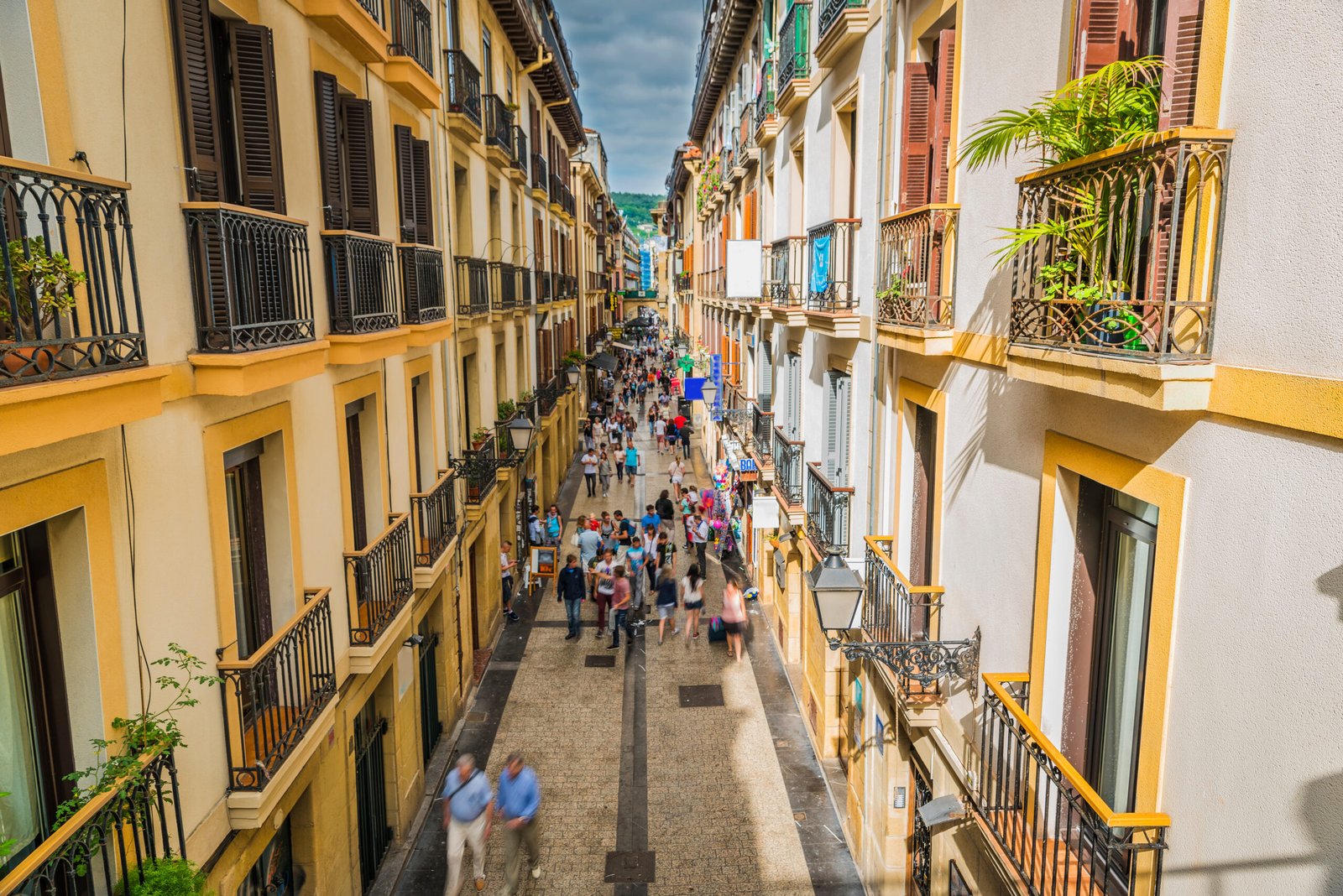 Crowds walking along a narrow pedestrian street in the Old Town of San Sebastián lined with balconies and pintxos bars