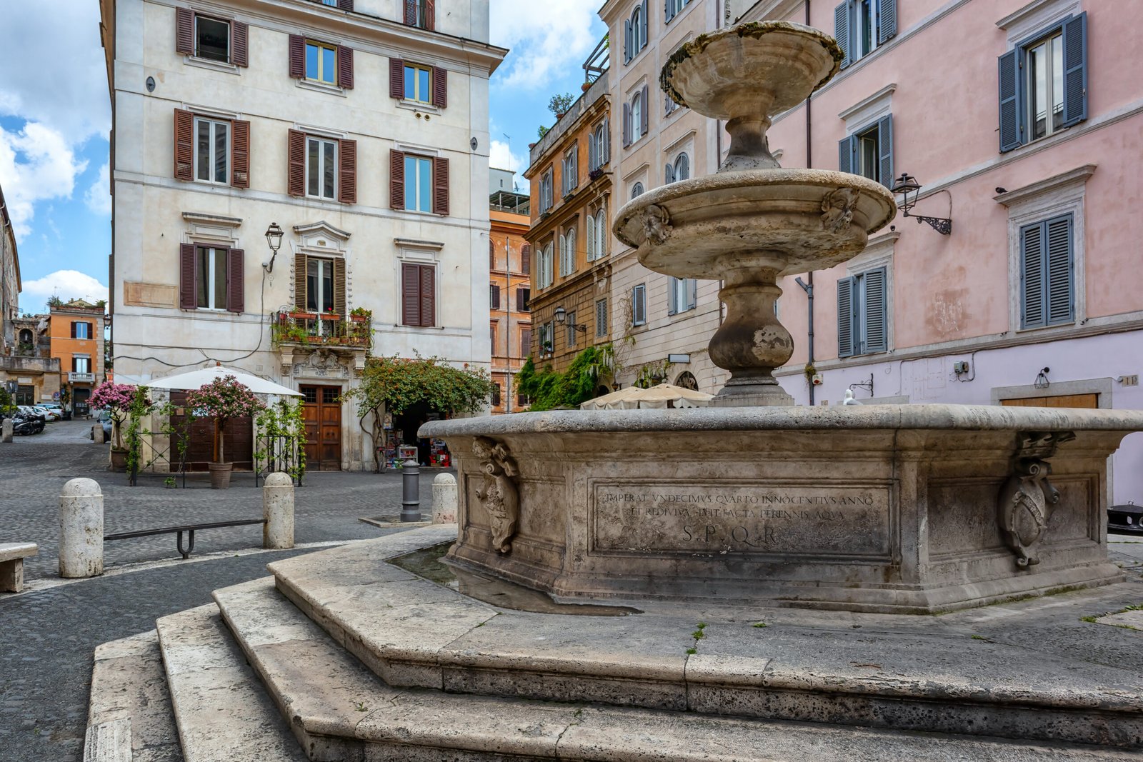 Fountain in Piazza della Madonna dei Monti in Rome surrounded by historic buildings and a small café