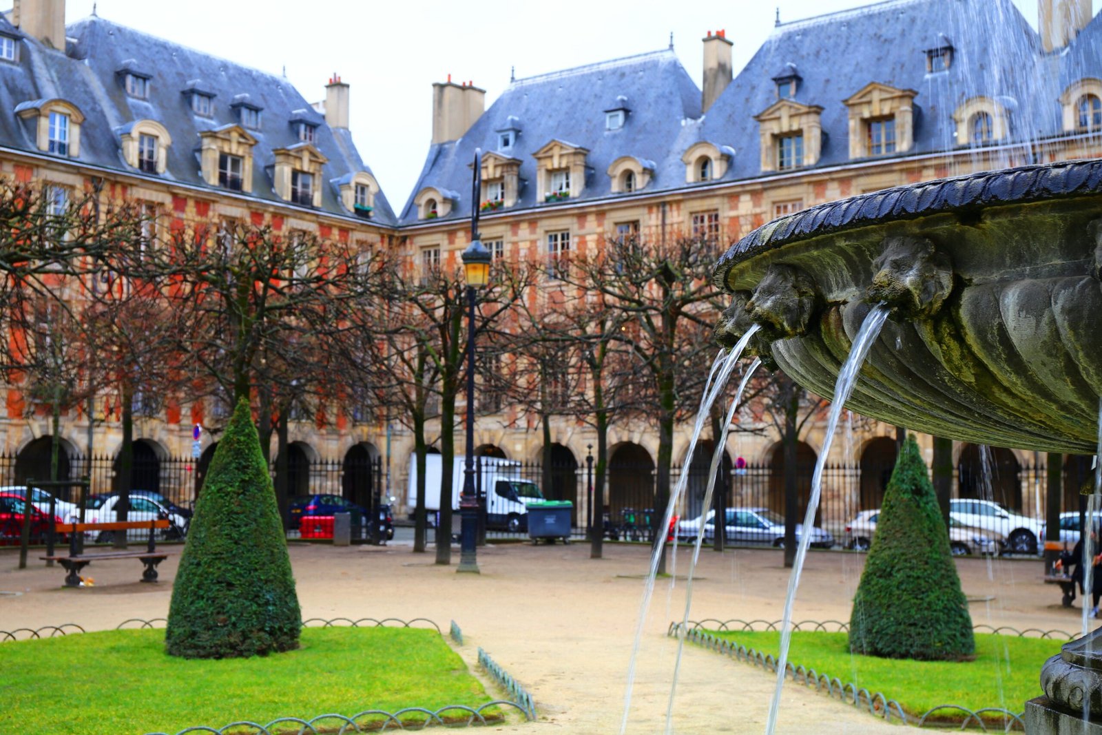 Fountain and manicured trees in Place des Vosges in the Le Marais neighborhood of Paris