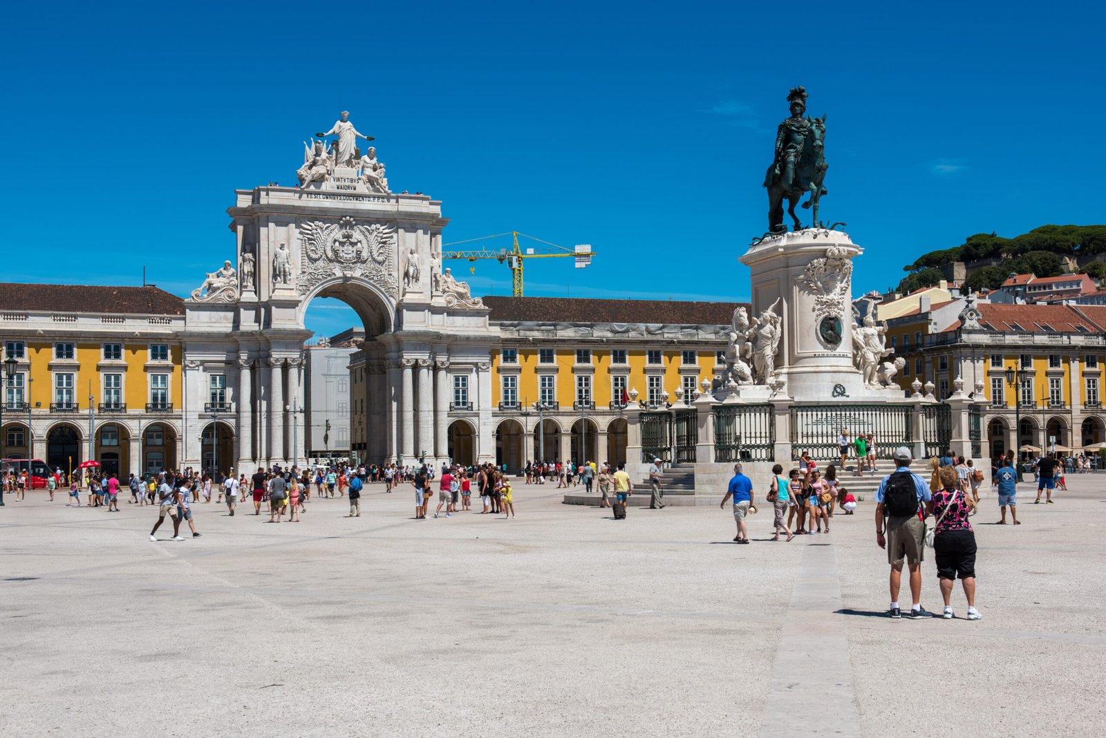 People walking across Praça do Comércio in Lisbon with the Rua Augusta Arch and equestrian statue on a sunny day