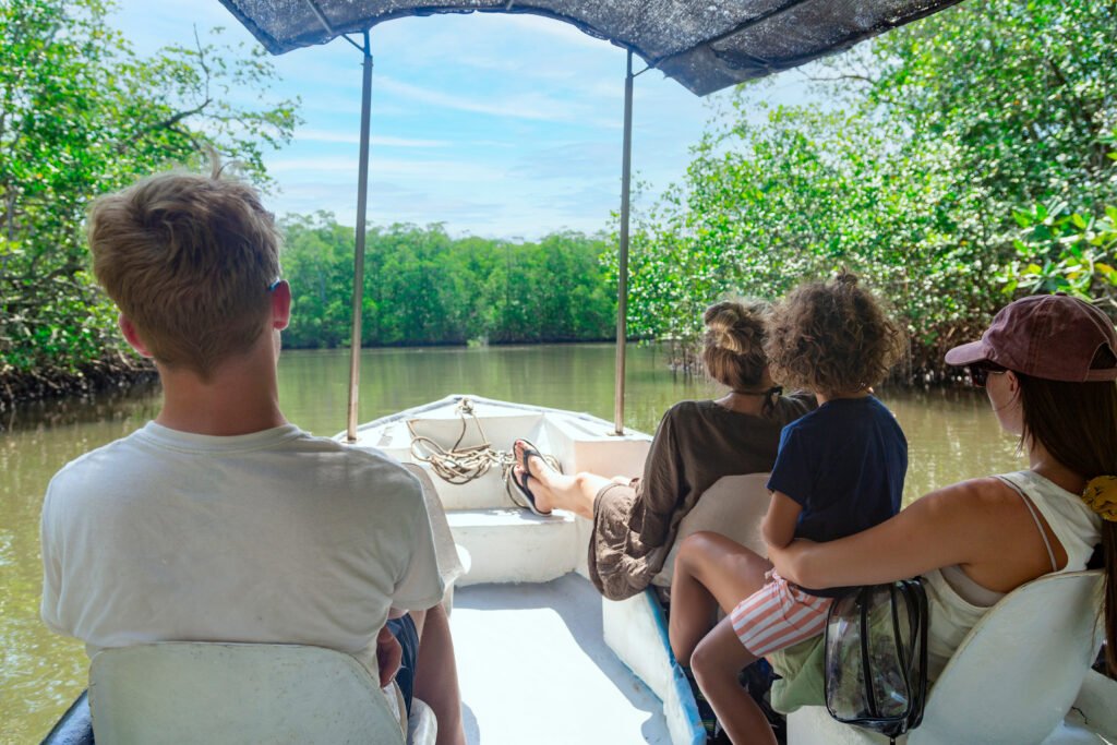 Family relaxing on a small boat drifting through green mangroves on Day 4 wildlife tour in Costa Rica.