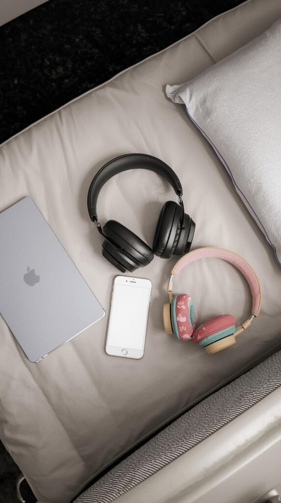 Adult over-ear headphones and colorful kids headphones next to a tablet and phone on a travel seat.