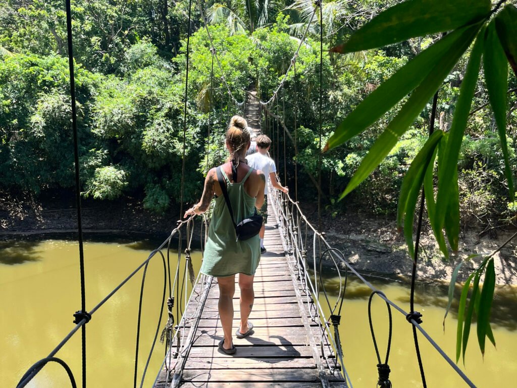Two visitors walking across a narrow suspension bridge over a lagoon in the jungle at Gumbalimba Park in Roatán.