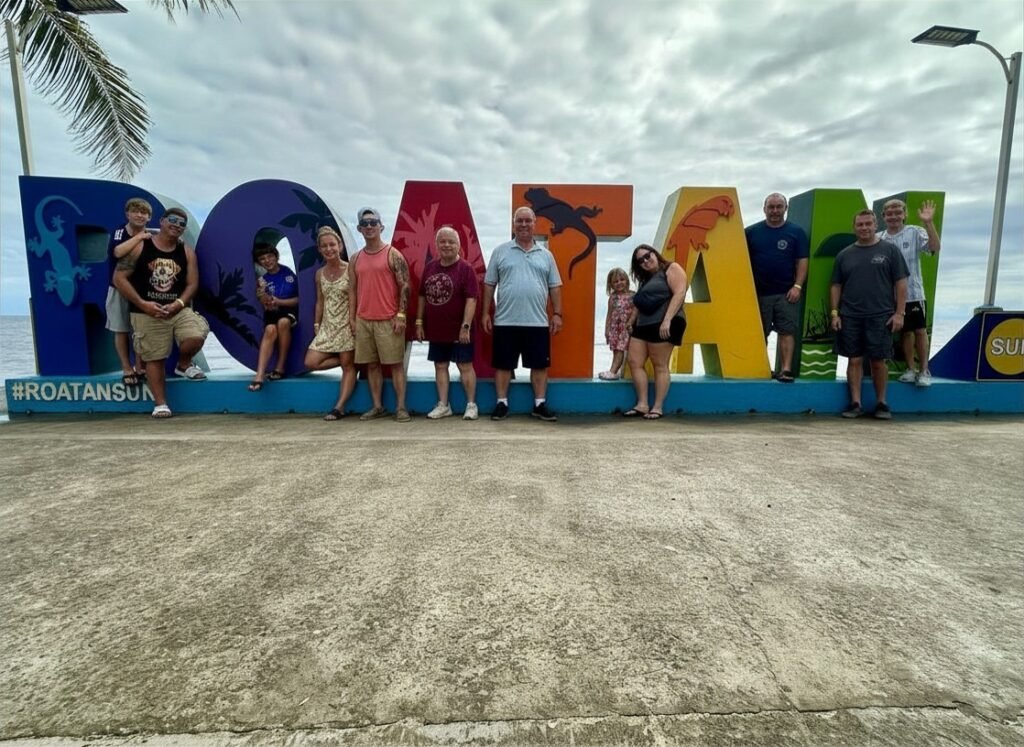 Multigenerational family posing together in front of the colorful Roatán sign on the waterfront.