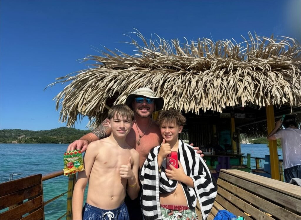 Smiling family on a tiki-style boat in Roatán, with clear blue water and thatched roof overhead during a day cruise.
