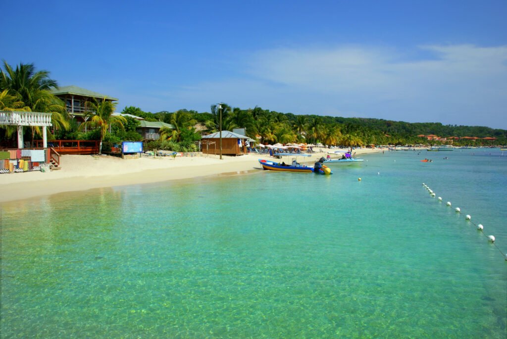 Wide view of West Bay Beach in Roatán with white sand, calm turquoise water, and small boats along the shore.