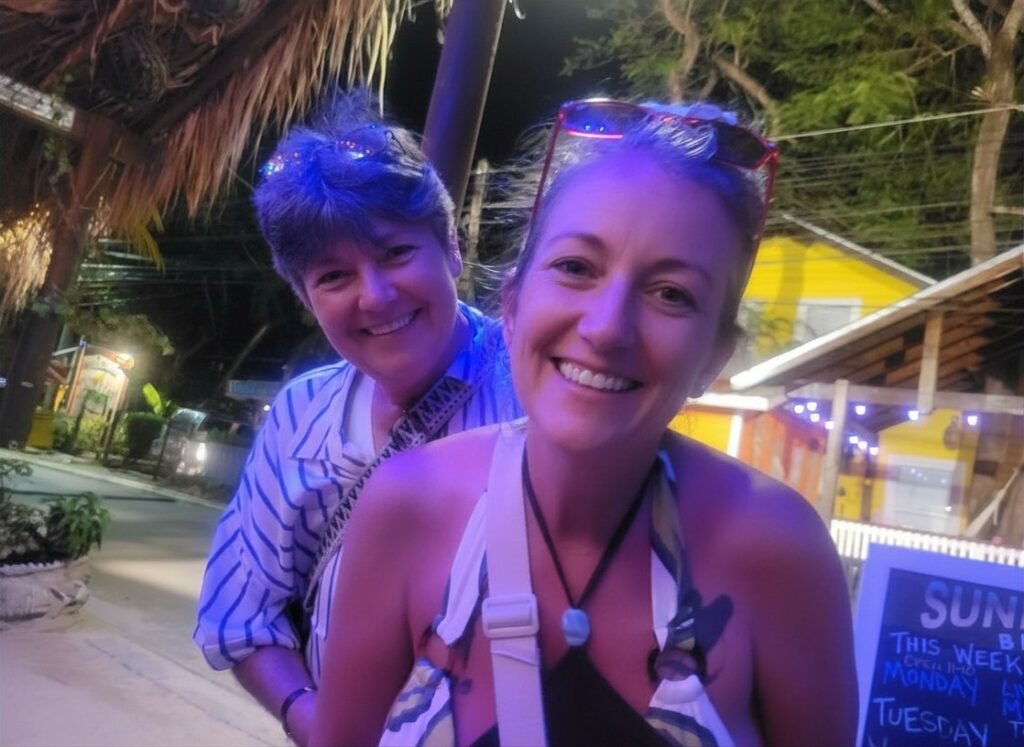 Two travelers smiling outside Sundowners beach bar in West End, Roatán, enjoying a relaxed evening drink.