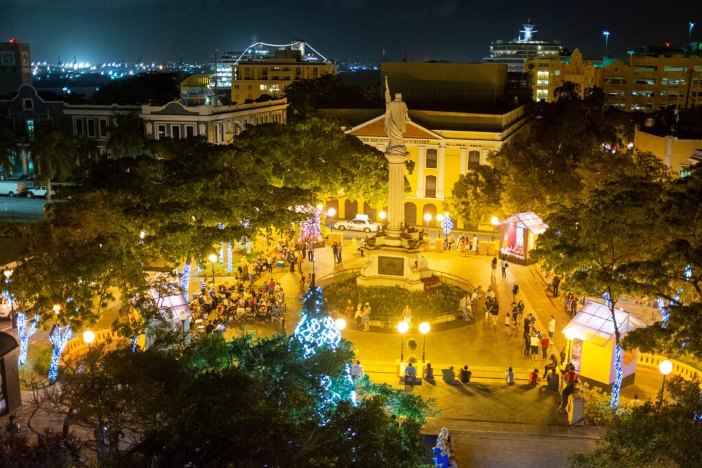 Holiday lights illuminate Plaza Colón as visitors gather in Old San Juan, Puerto Rico, at night.