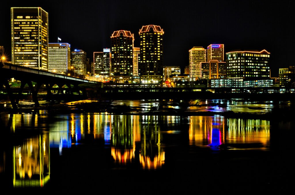 Illuminated downtown Richmond skyline reflected in the James River at night.