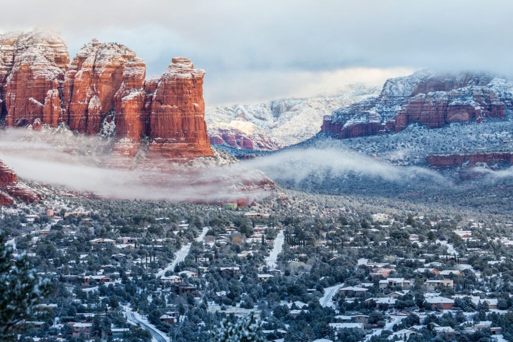 Snow-dusted red rock formations rise above Sedona, Arizona, on a misty winter day.
